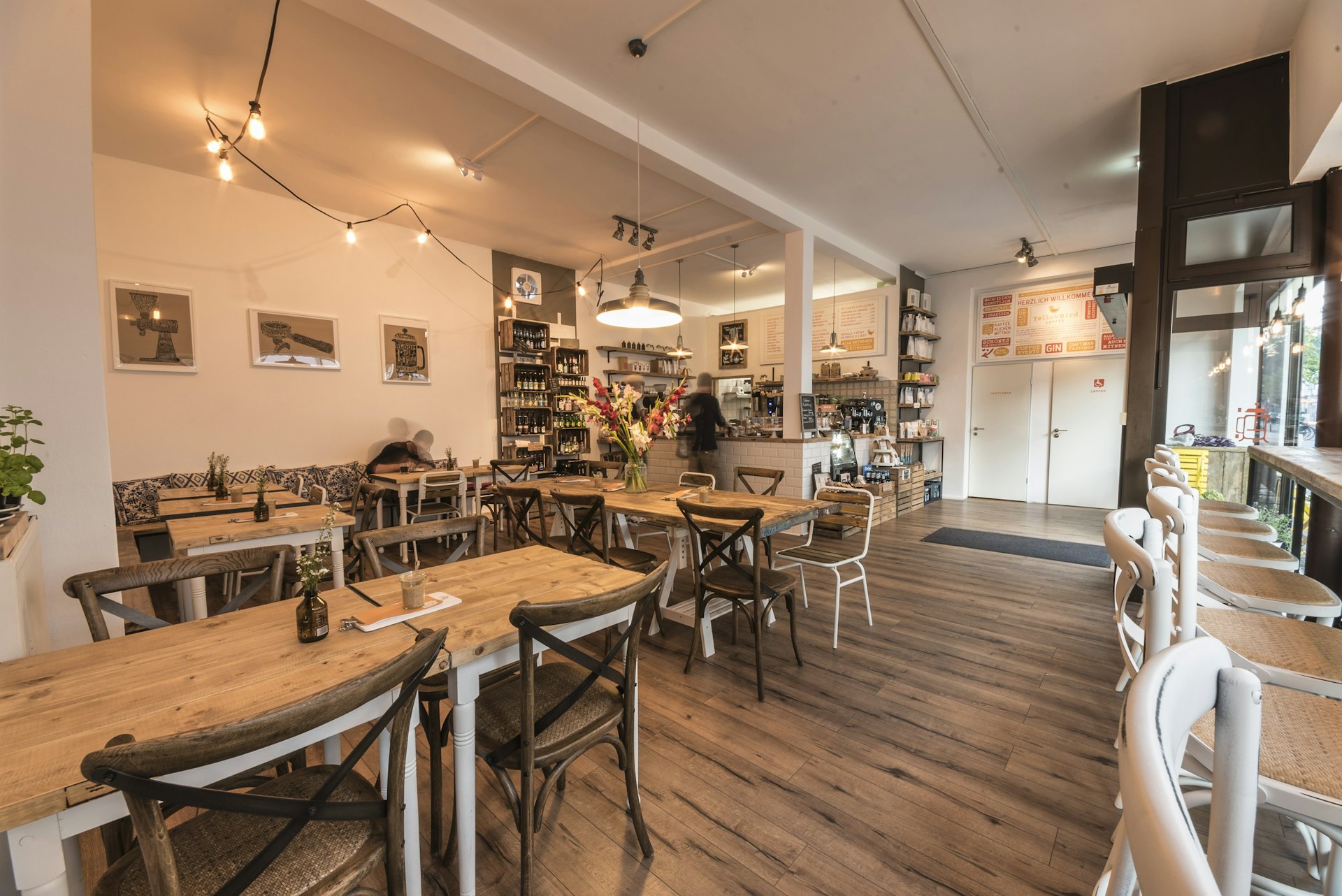 Ahşap masa ve sandalyelerle düzenlenmiş beyaz duvarlı kafe iç mekânı
